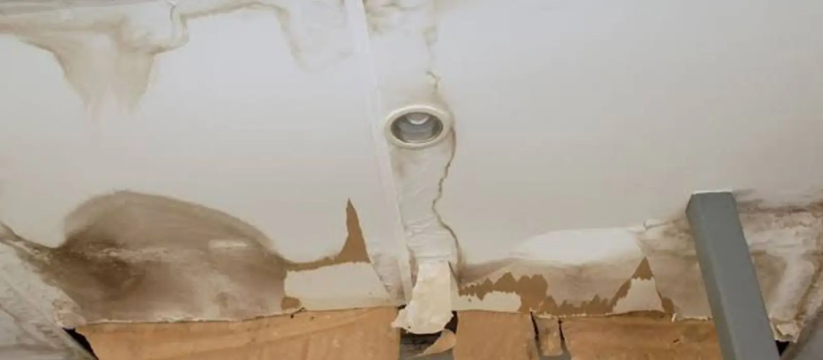 Water-stained ceiling with peeling paint and brown stains around a ceiling vent