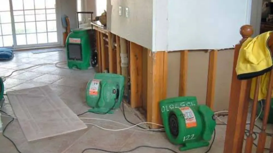 Green air movers drying a room where the lower drywall has been cut out